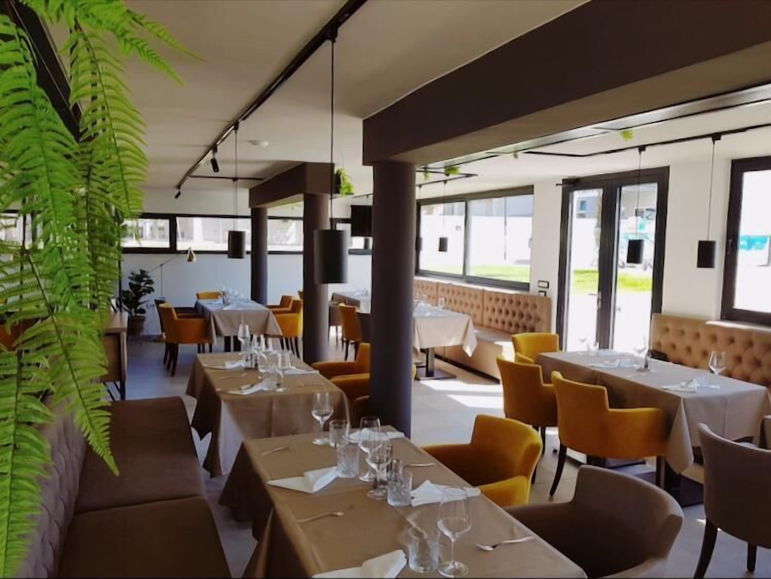 A restaurant with tables set for dining, yellow chairs, and large windows allowing natural light.