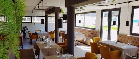 A restaurant with tables set for dining, yellow chairs, and large windows allowing natural light.