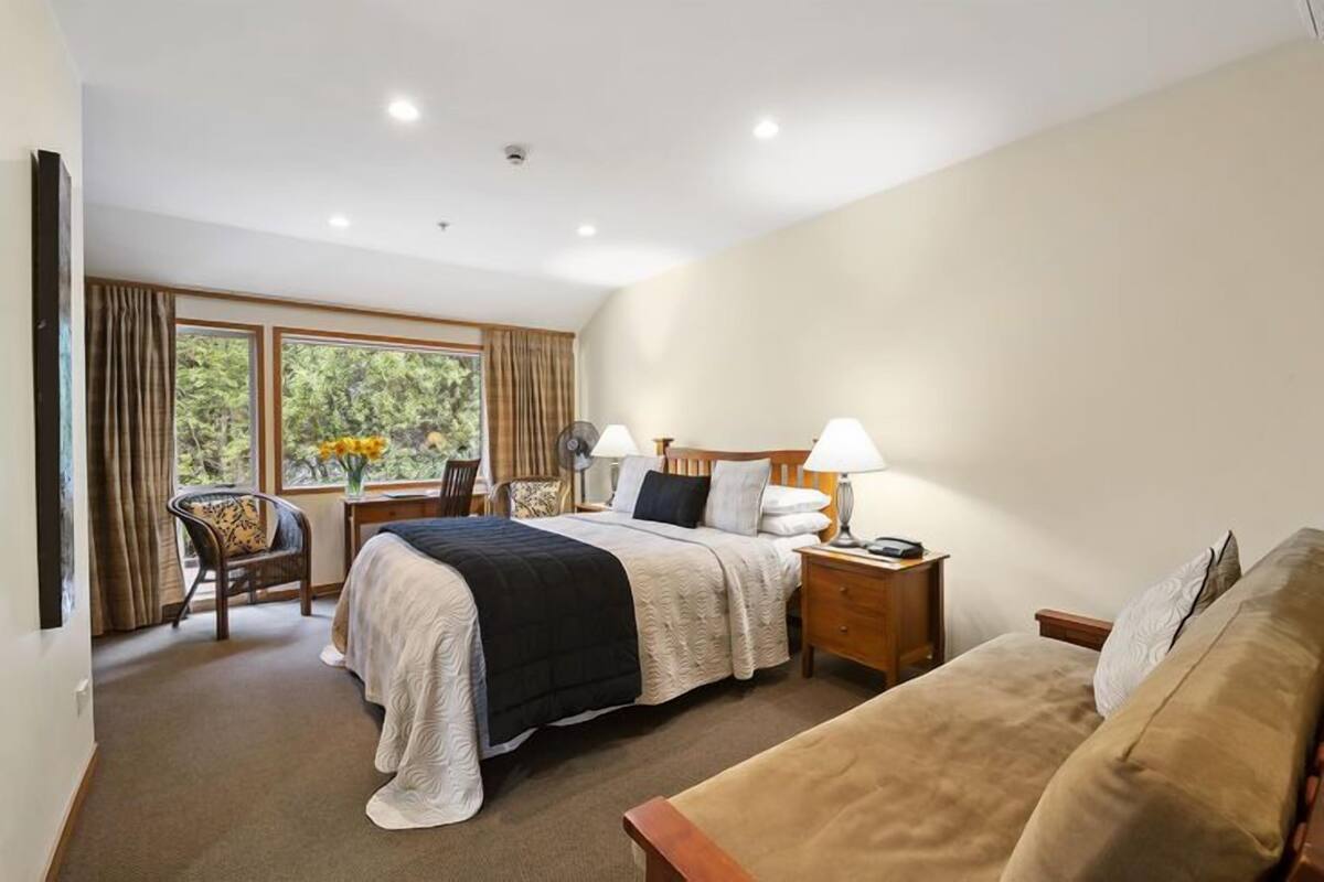 Habitación de hotel con cama, mesitas de noche, una silla, un sofá y una ventana con cortinas.