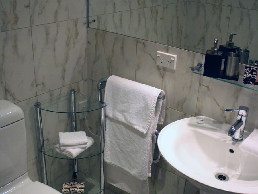 Un baño con inodoro, lavabo, estantes de vidrio y un cubo de basura.