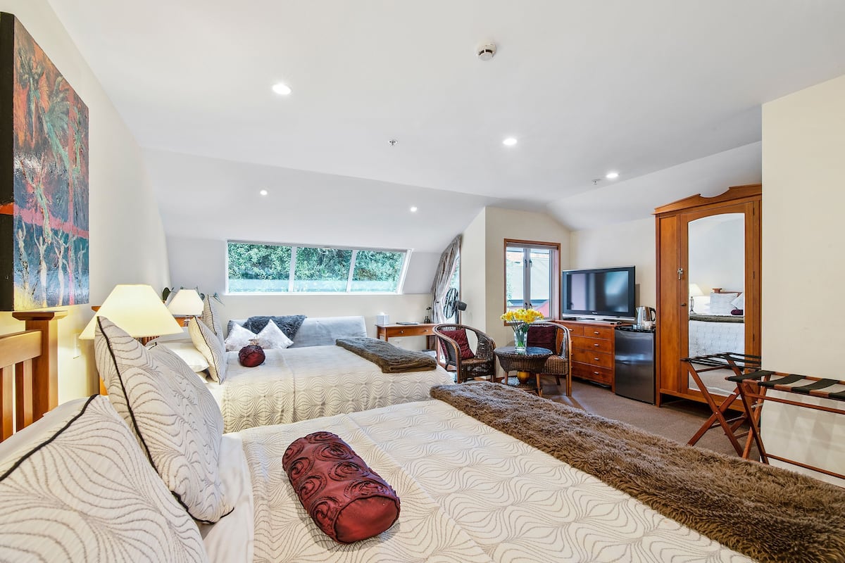 Una habitación de hotel moderna con dos camas, un comedor, un televisor y un ventanal grande.