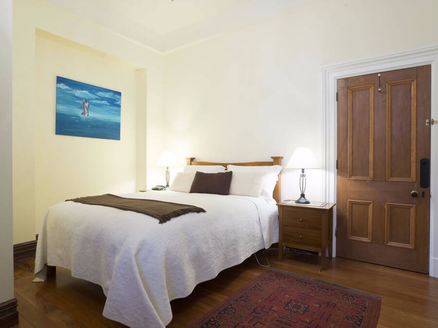 Un dormitorio ordenado con cama, lámparas de noche, una puerta de madera y un cuadro en la pared.