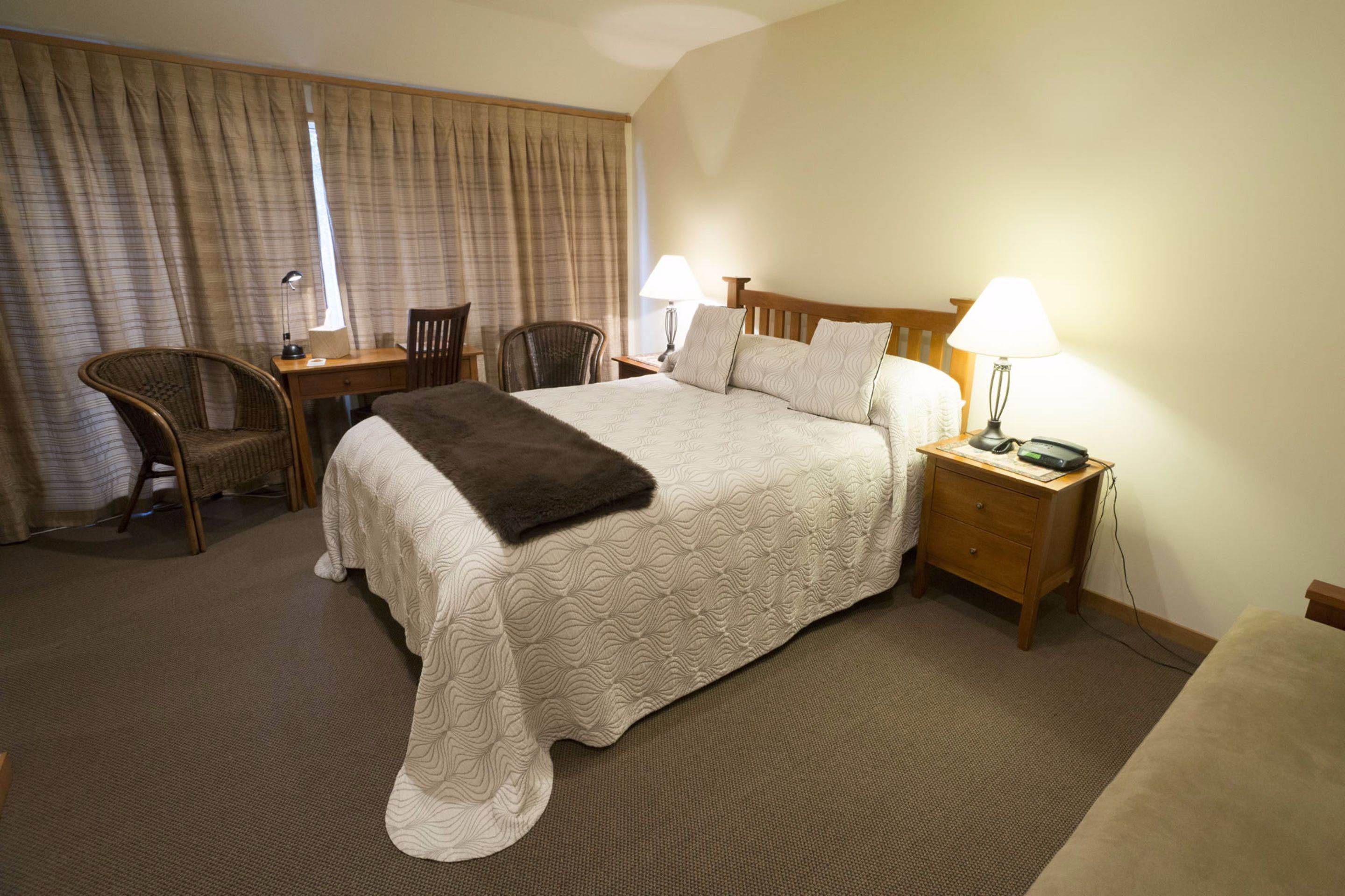 A hotel room with a large bed, two bedside tables with lamps, a chair, and a desk.