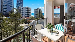 A balcony with a table, chairs, and a view of tall buildings and the ocean. - Marrakesh Apartments (Surfers Paradise)
