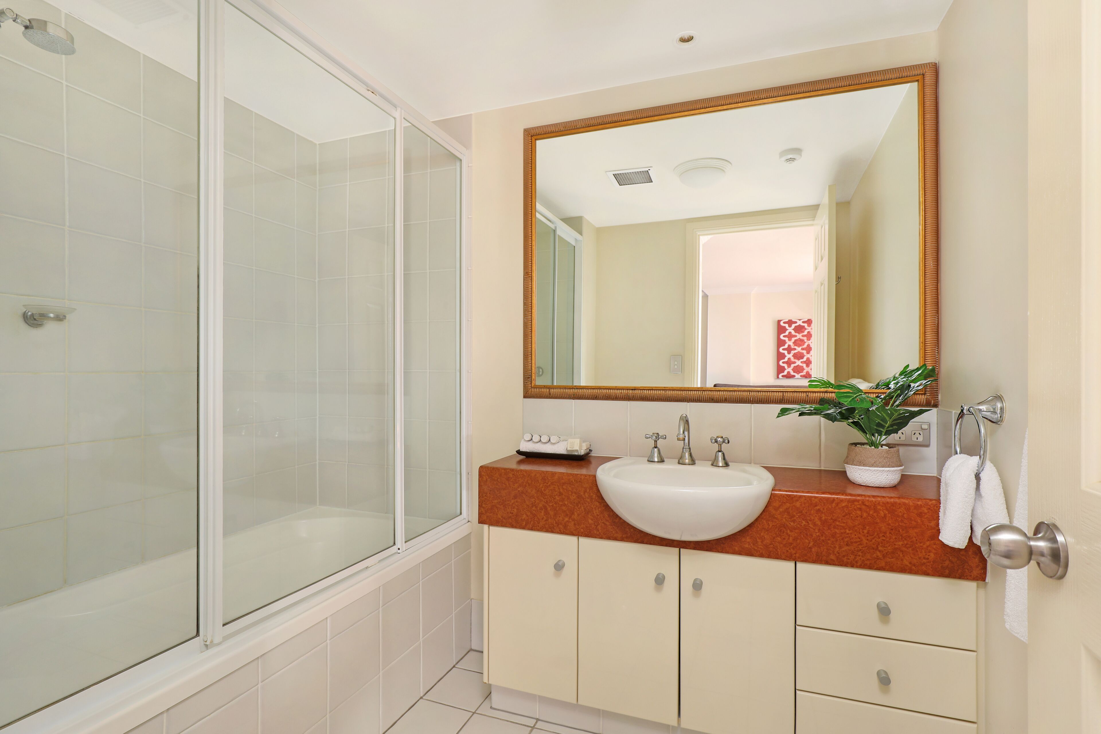 Een badkamer met een douchecabine van glas, een wastafel met spiegel erboven en een handdoekrek.