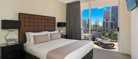 Habitación de hotel con una cama grande, dos mesitas de noche con lámparas, vistas de la ciudad desde un balcón y un ventilador de techo.