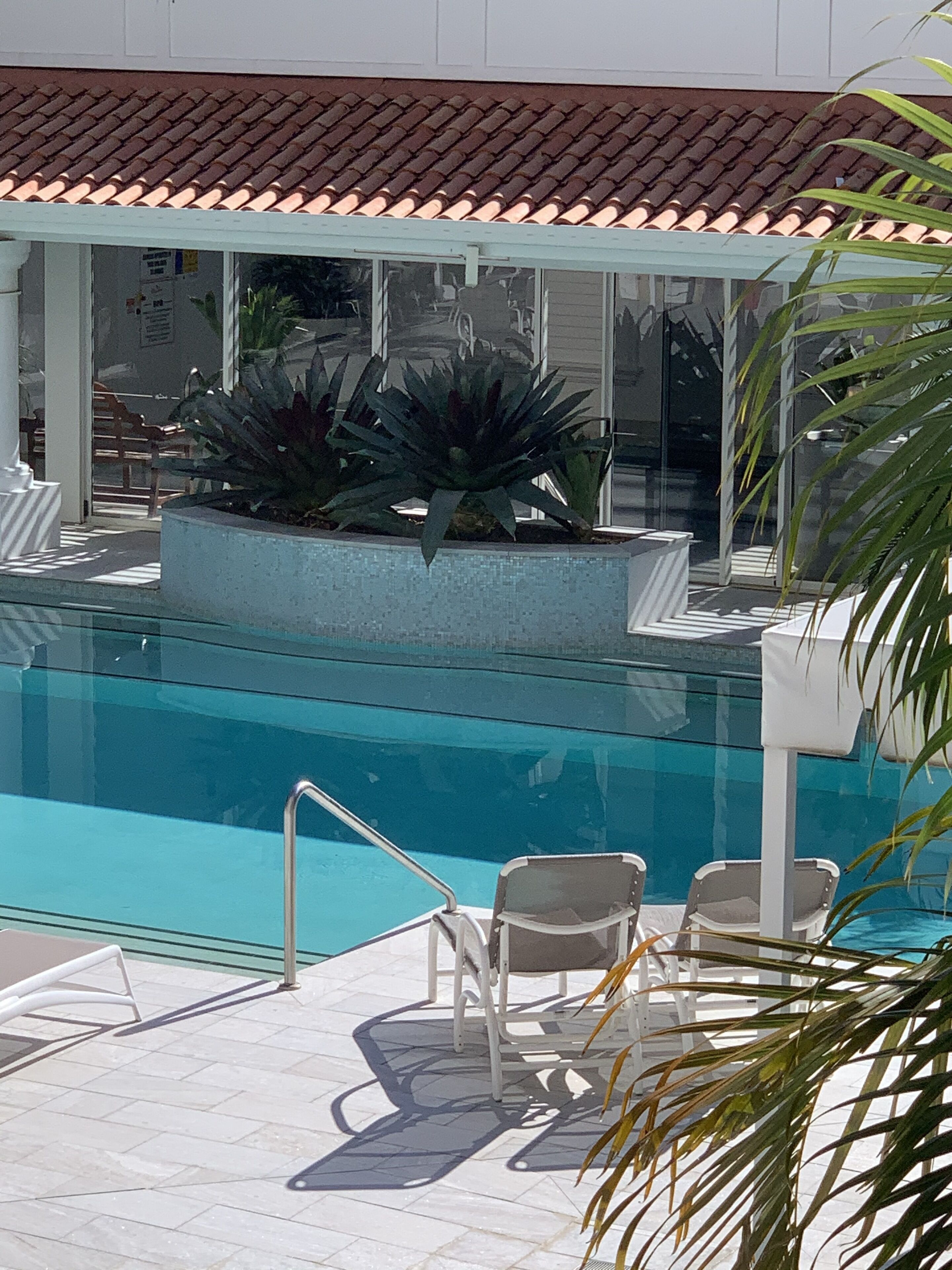 A swimming pool with a tiled deck, lounge chairs, and potted plants.