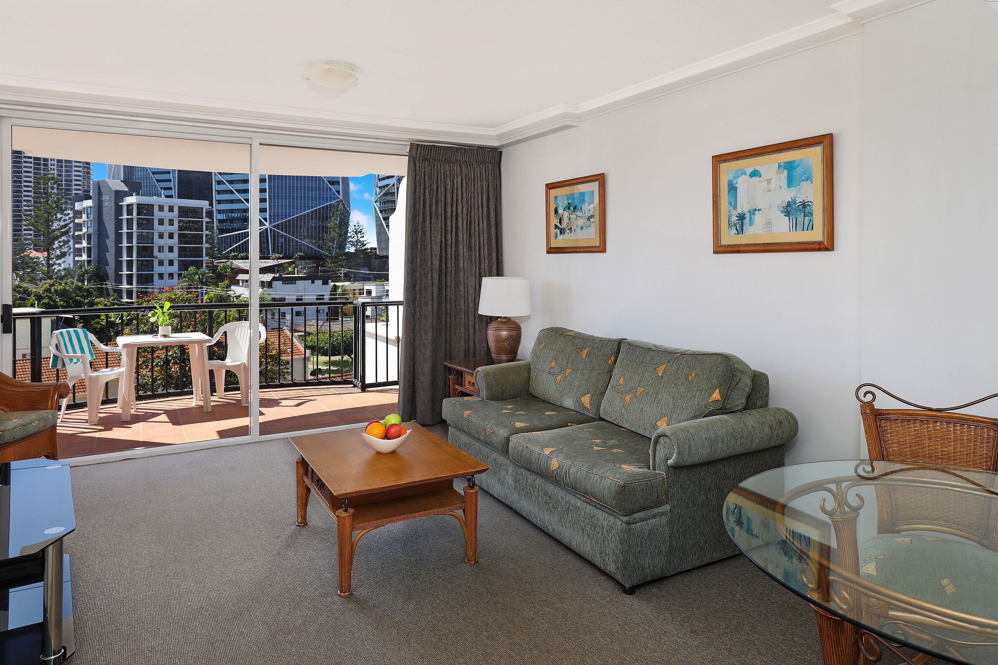 A living room with a sofa, a glass table, and a balcony with outdoor furniture.