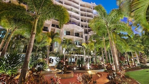 A multi-story hotel with a central courtyard, palm trees, and a fountain. - Marrakesh Apartments (Surfers Paradise)
