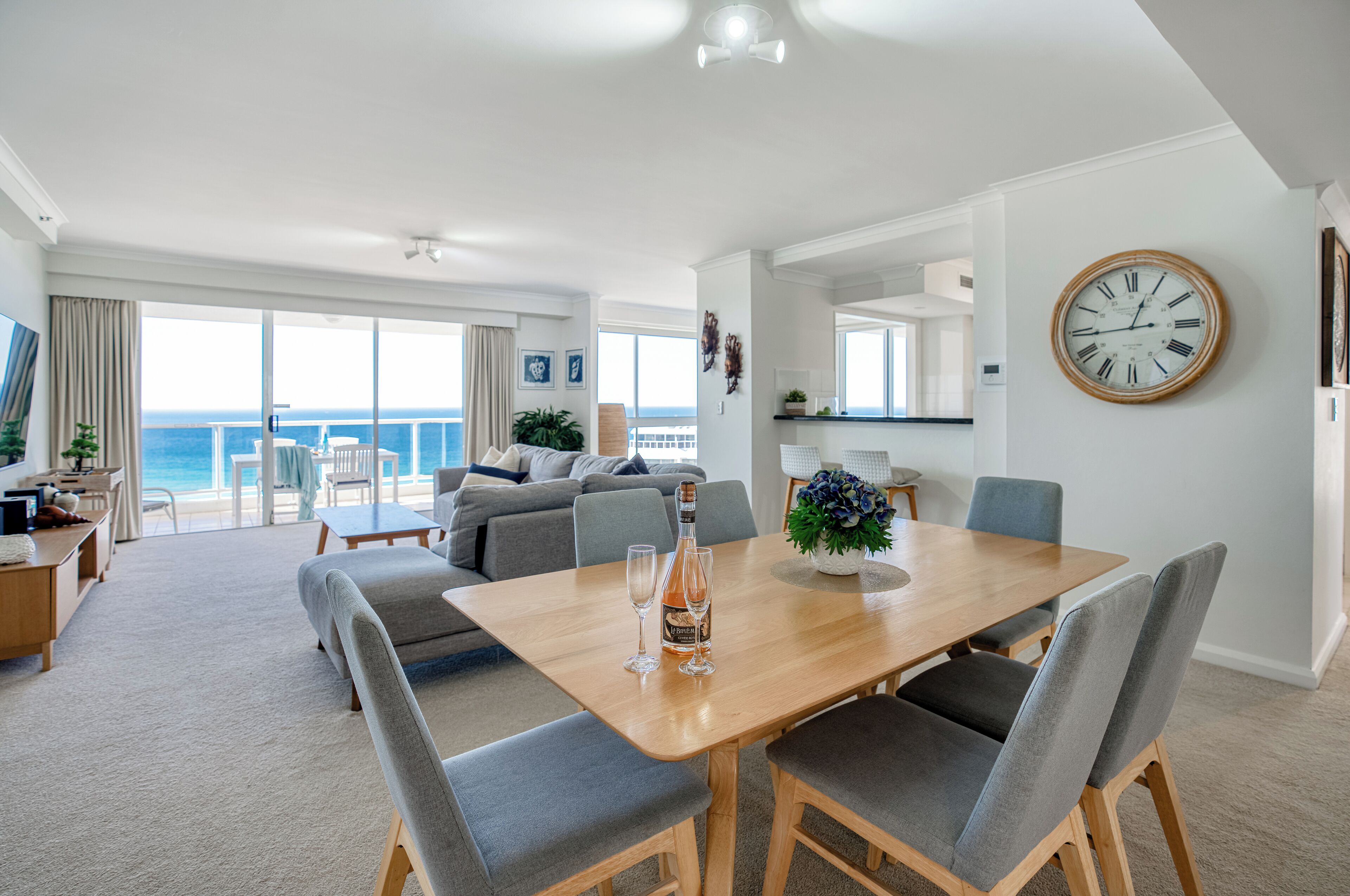 A modern living room with a dining area, large windows, and a view of the ocean.