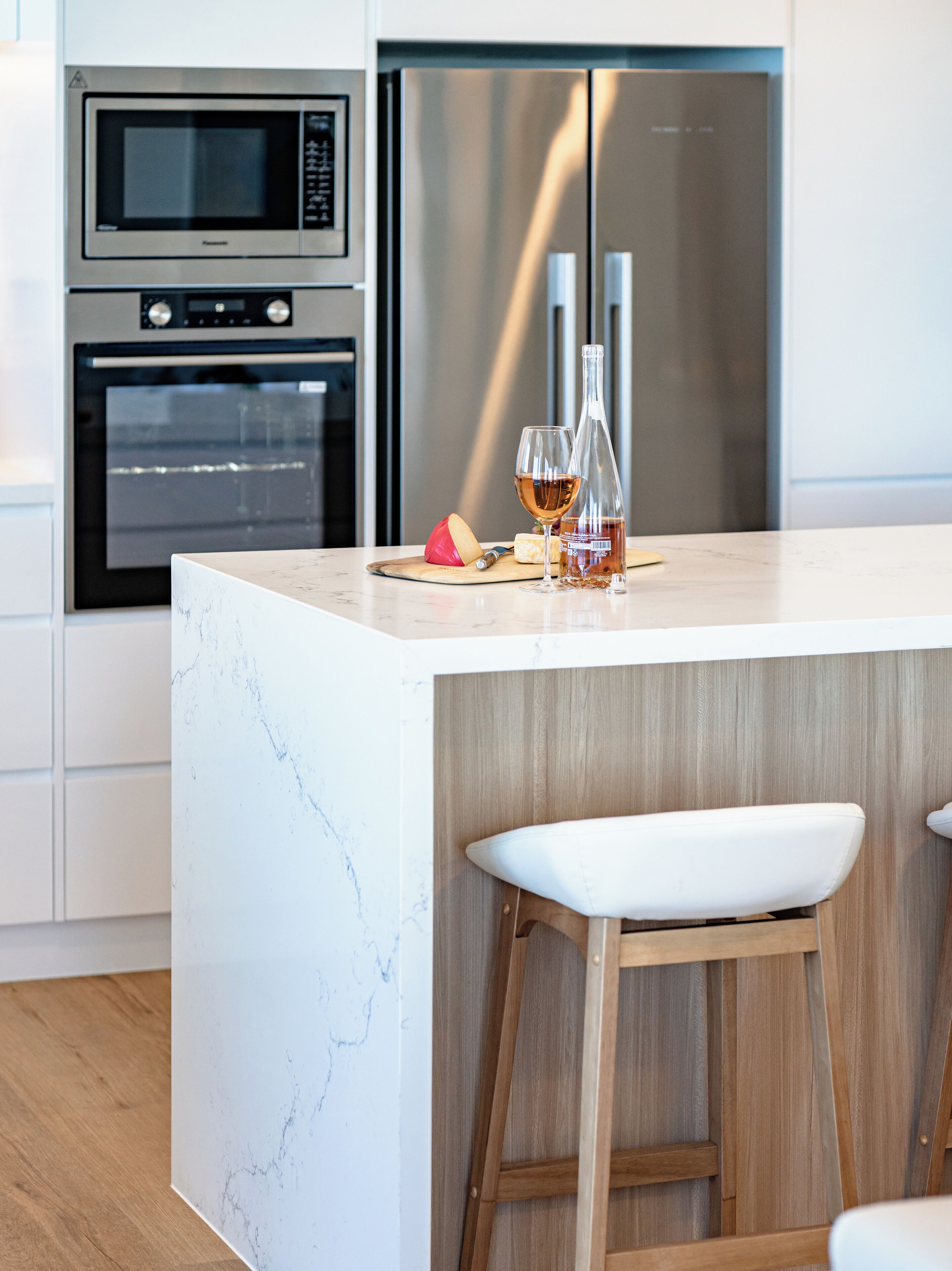 A modern kitchen with a marble countertop, stainless steel appliances, and wooden stools.