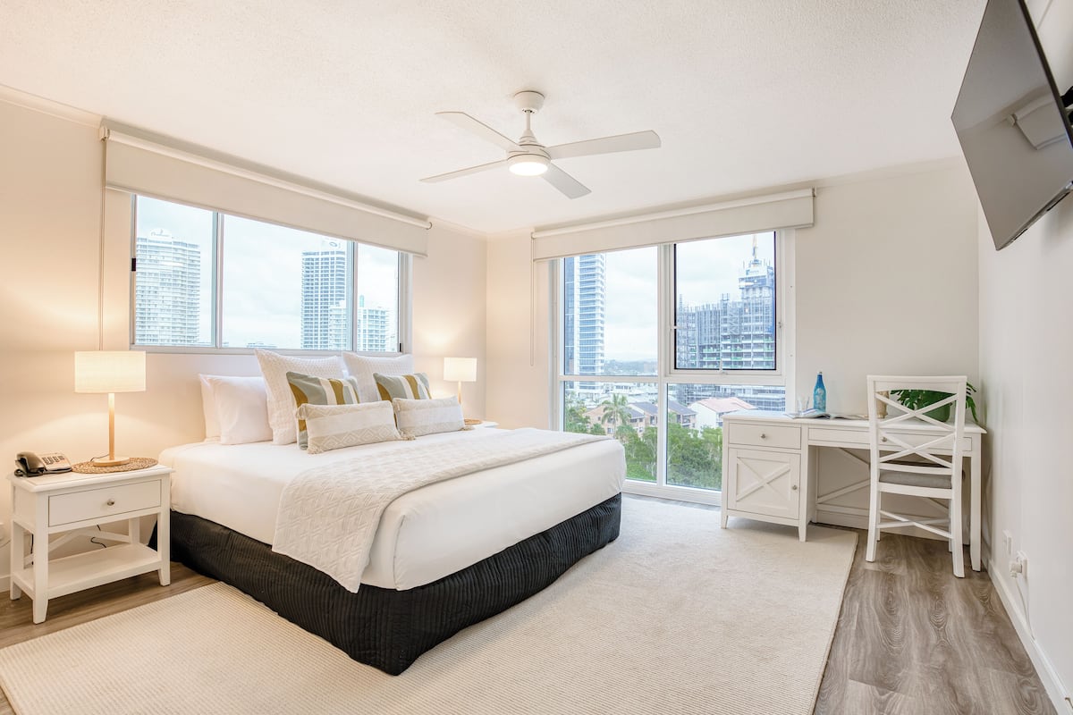 A modern bedroom with a large bed, a desk, and a view of the city.