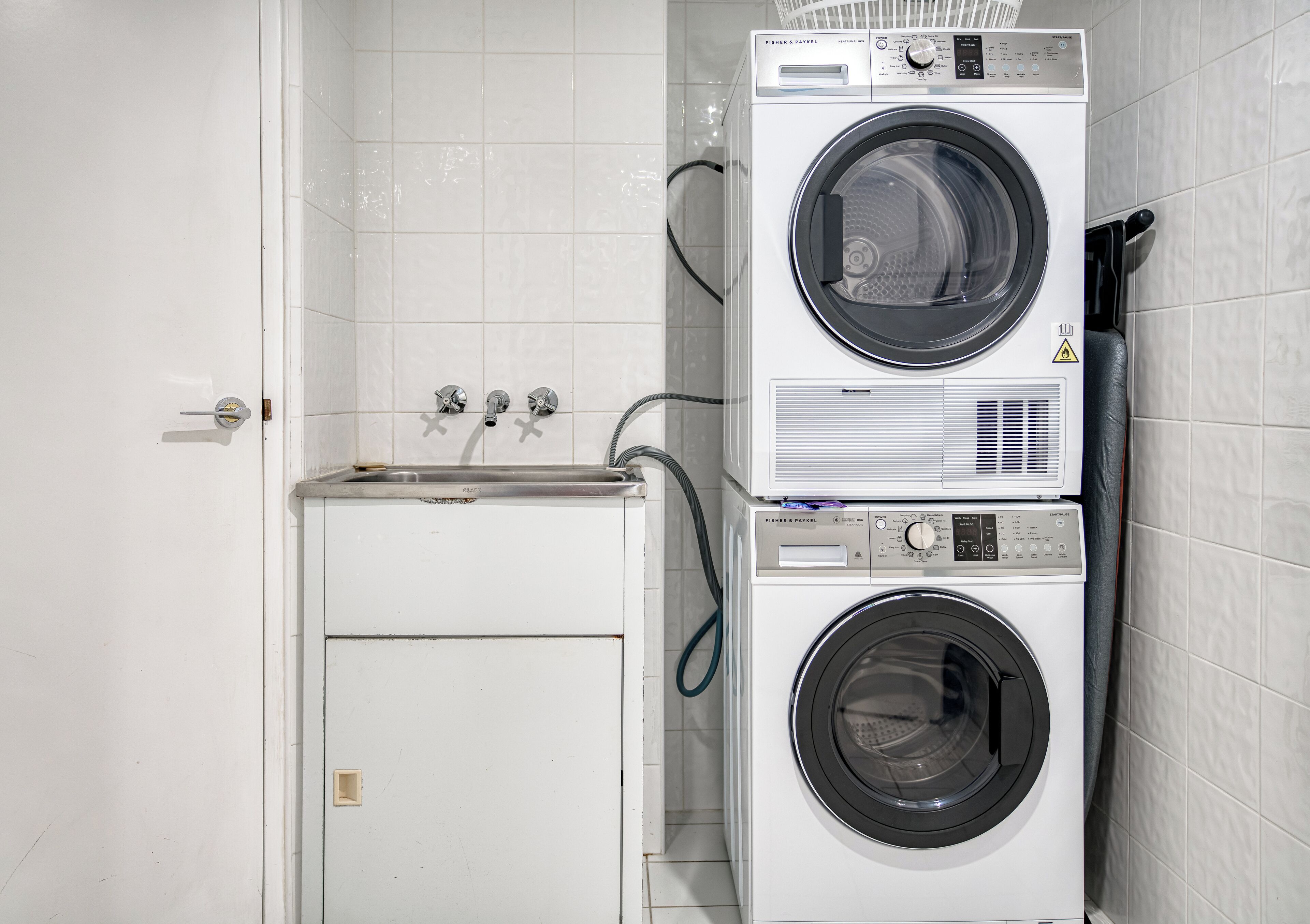 A laundry area with a front-loading washer and dryer, a sink, and a towel rack.