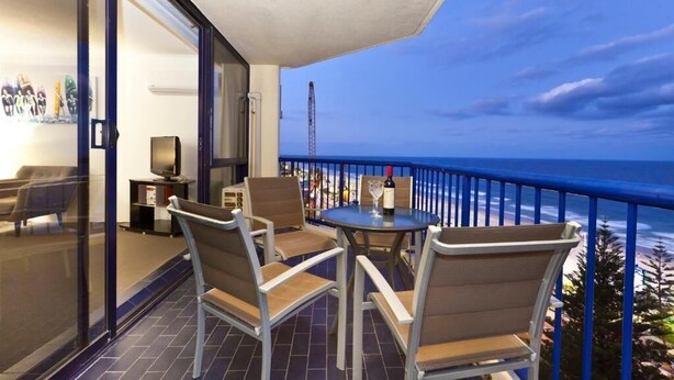 A balcony with a table and chairs, a TV, and a view of the ocean. - Surf Regency Apartments (Surfers Paradise)