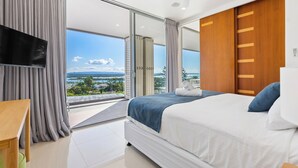 Une chambre d’hôtel moderne dotée d’un grand lit, d’une télévision à écran plat et d’un balcon offrant une vue sur l’océan.