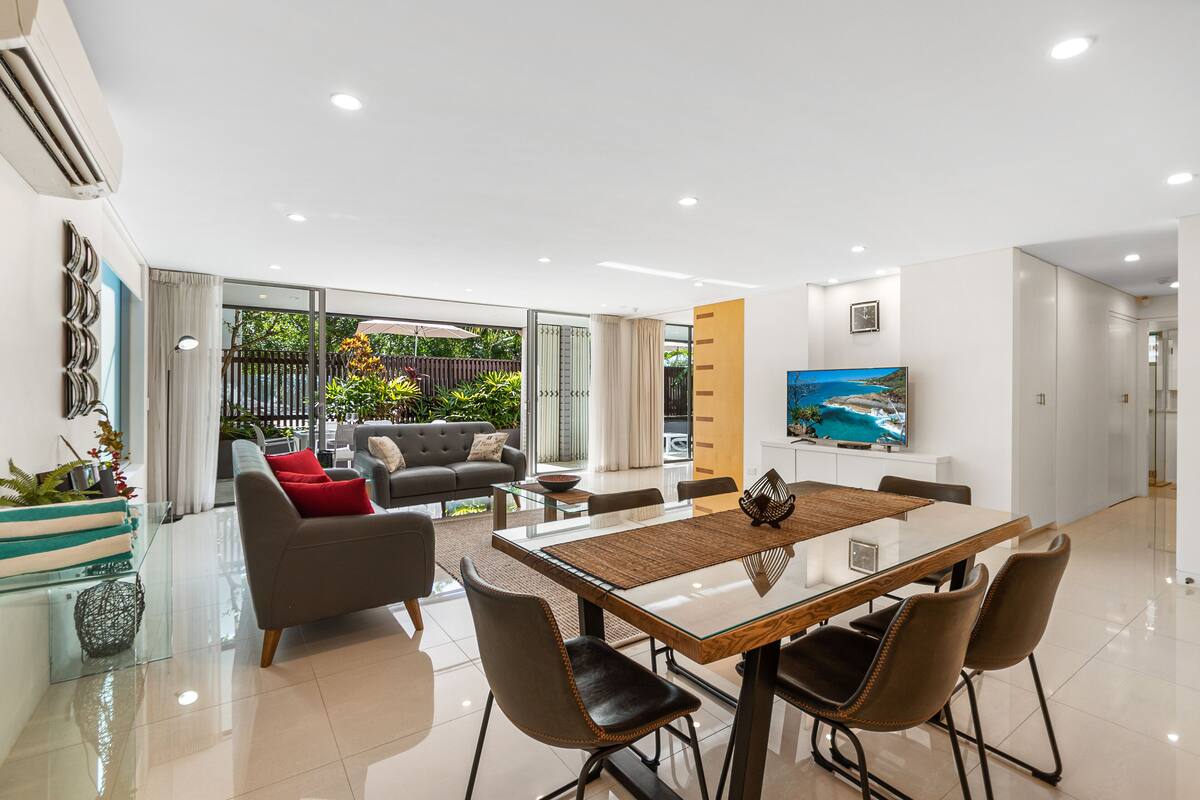 A modern living room with a dining area, large windows, and a flat-screen TV.