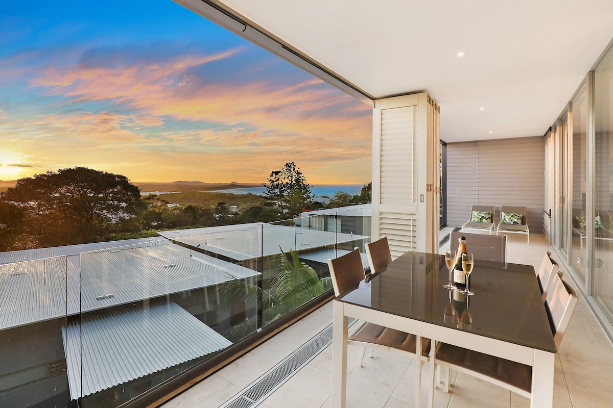 A modern balcony with a glass table, two chairs, and a bottle of wine.