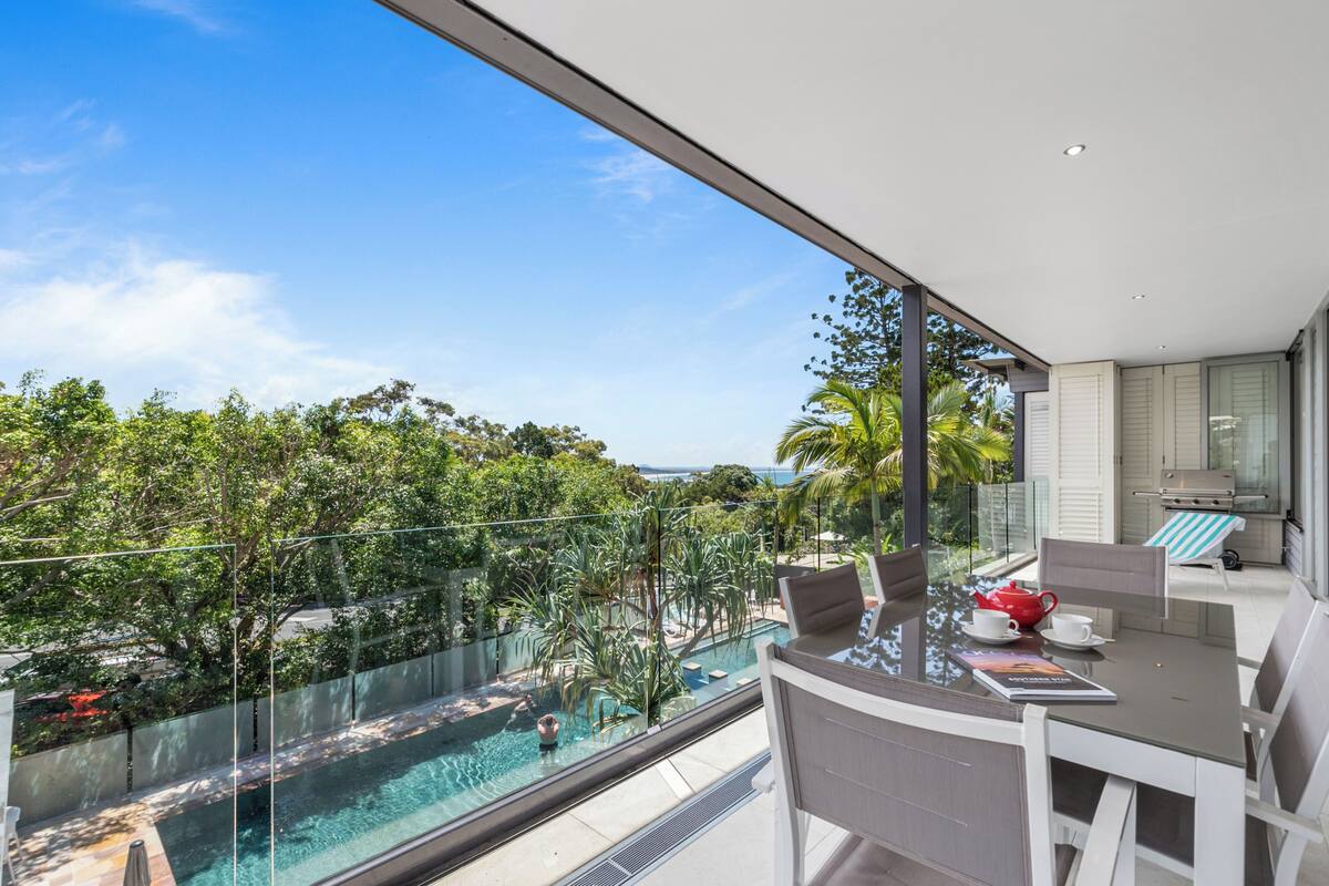 A balcony with a glass barrier overlooking a swimming pool and lush greenery.