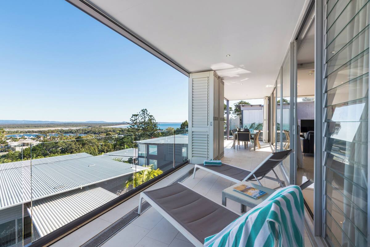 A modern balcony with a view of the city and ocean, furnished with lounge chairs and a table.