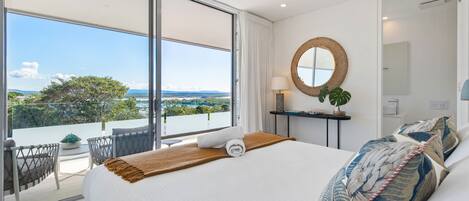Habitación de hotel con una cama grande, vistas al exterior, un espejo redondo y una pequeña mesa con una planta.