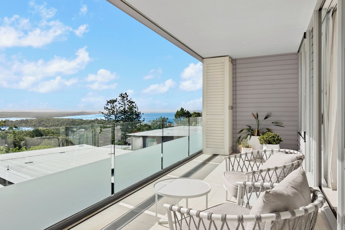 A balcony with a glass railing, a white table, and a cushioned chair.