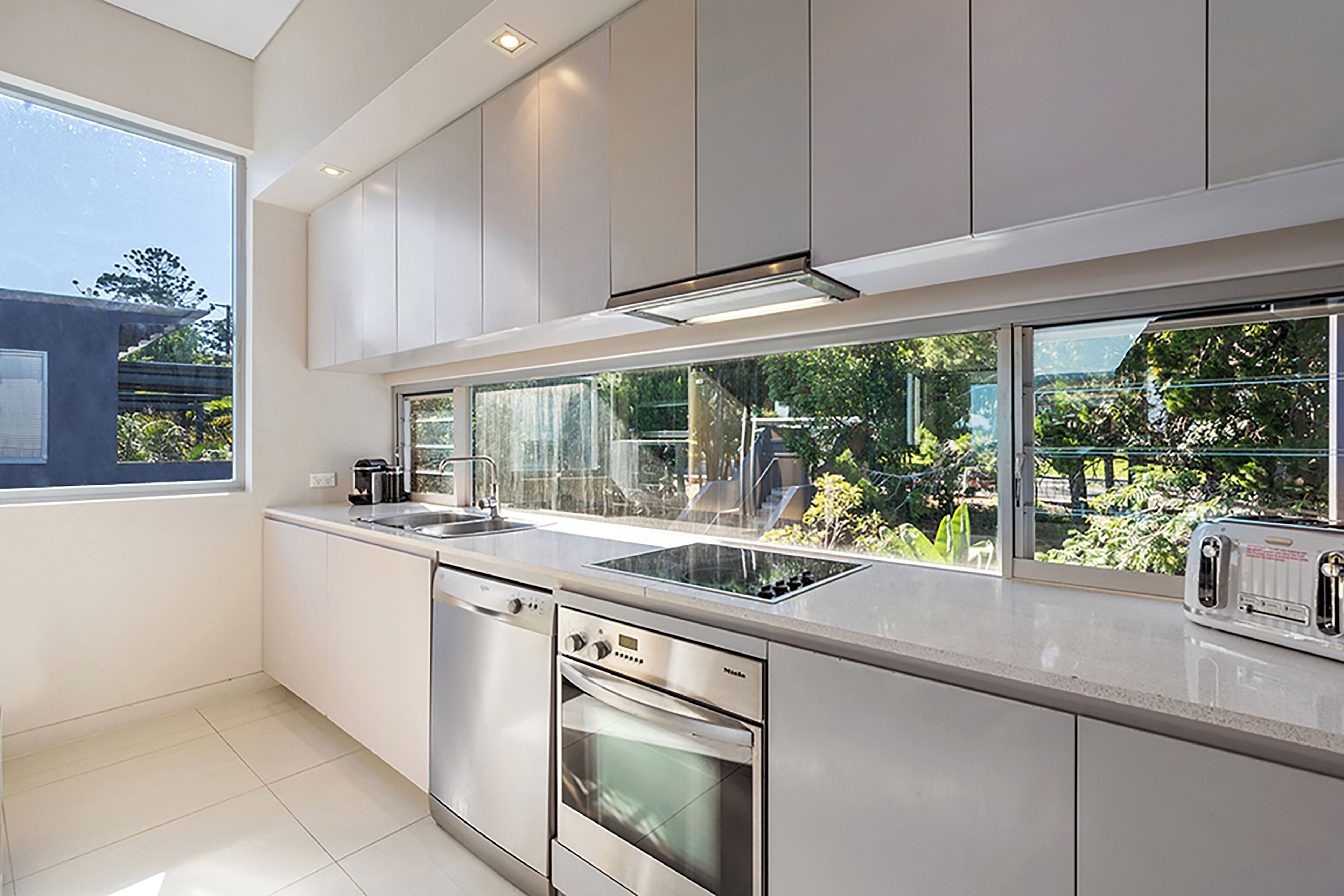A modern kitchen with stainless steel appliances, a large window, and a view of greenery outside.