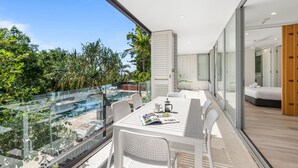 Un balcon moderne avec une balustrade en verre, des meubles blancs et une vue sur une piscine et un espace verdoyant.