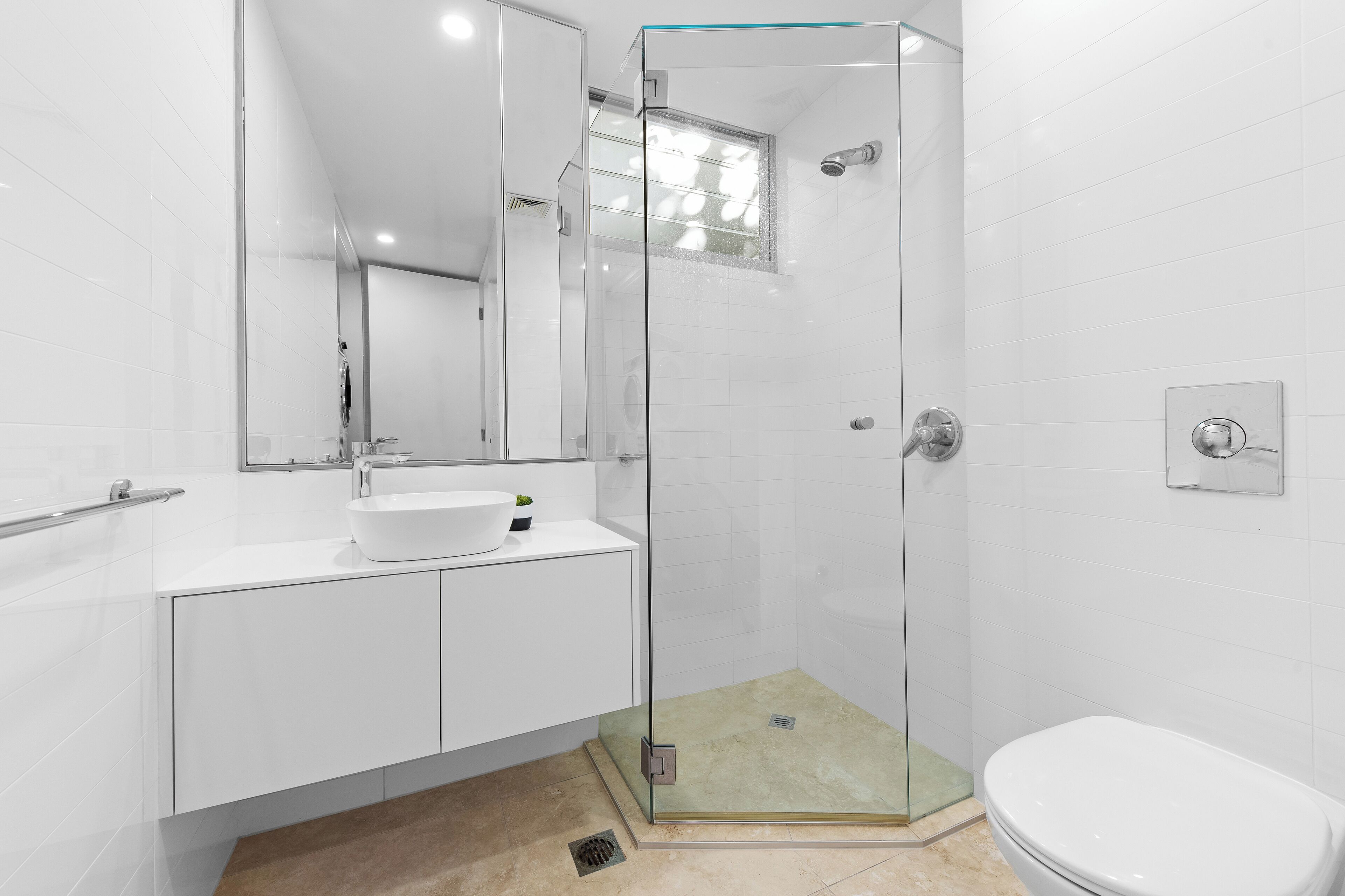 Een moderne badkamer met een douchecabine van glas, een wit wastafelmeubel en een toilet.