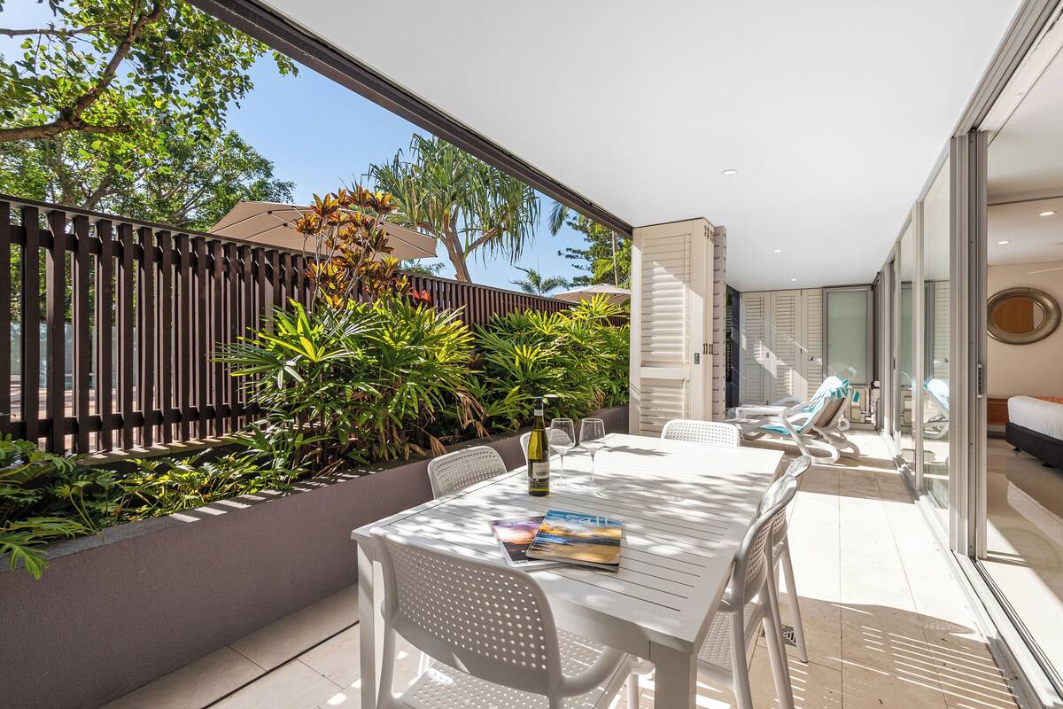 A modern outdoor dining area with a white table and chairs, a bottle of wine, and a menu.