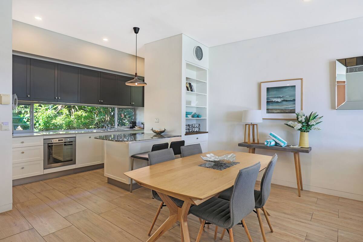 A modern kitchen with dark cabinets, a wooden dining table, and a built-in island with seating.