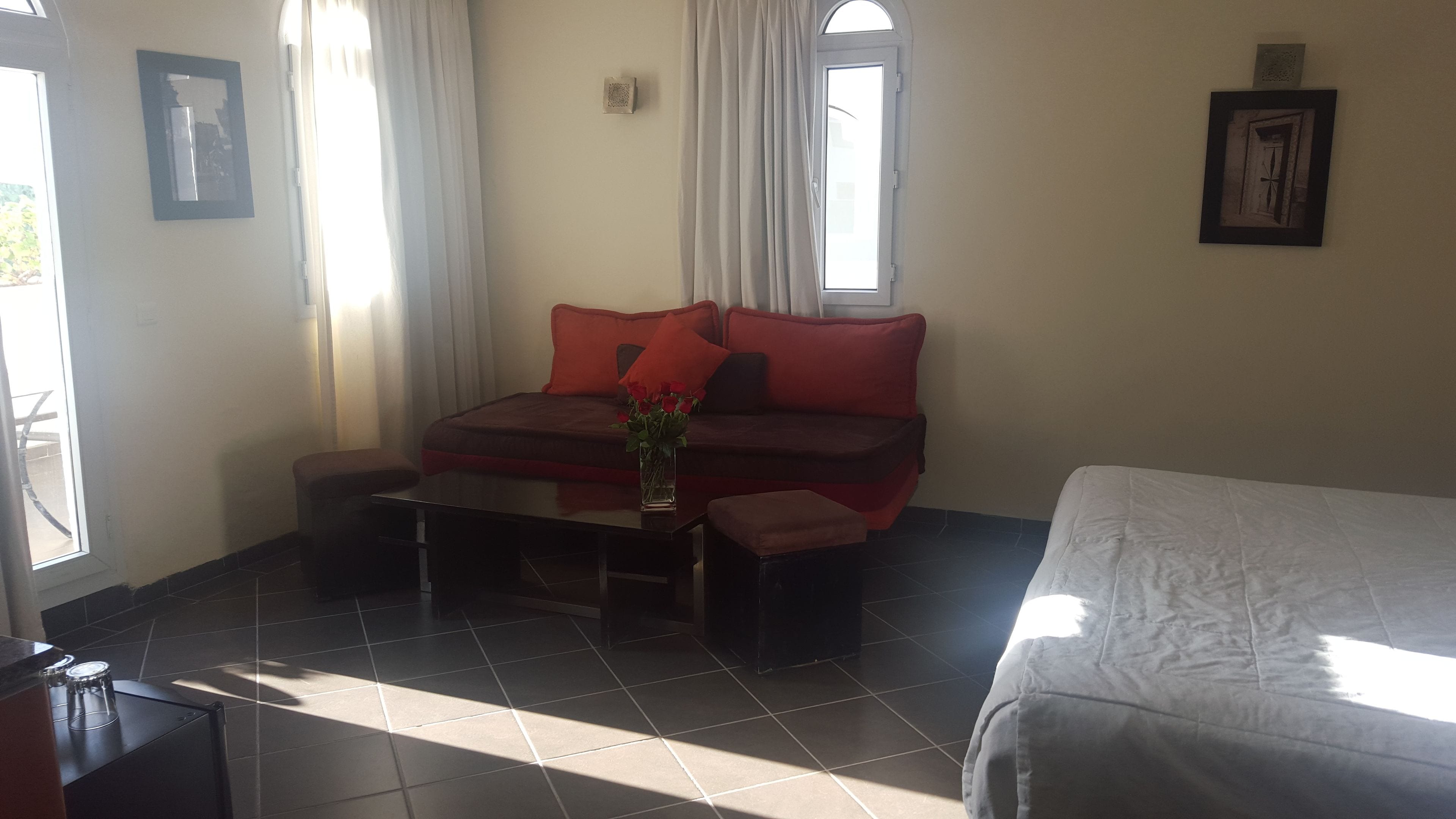 A room with a bed, a sofa, a small table with a vase of flowers, and a window with curtains.