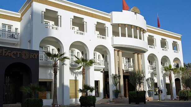 A white building with multiple balconies and arched doorways, featuring a sign for 'The Factory'.