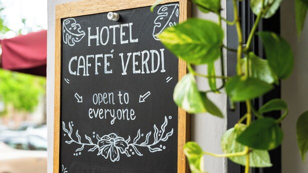 A chalkboard sign with 'HOTEL CAFFÈ VERDI' and 'open to everyone' written on it.