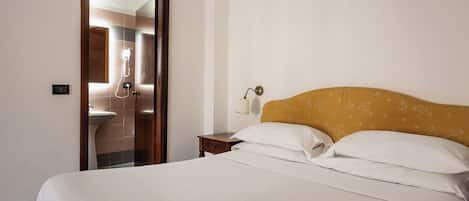 Een hotelkamer met een bed, nachtkastje, lamp en een badkamer, zichtbaar door een glazen deur.