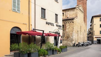 Un hôtel avec un auvent rouge, des tables à l’extérieur et un scooter garé.