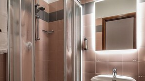 A shower enclosure with a glass door, a sink with a pedestal base, and a mirror above the sink.