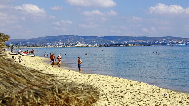 A beach with people walking and swimming, a clear sky, and distant hills. - Hello Yasmine Hotel (Hammamet)
