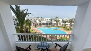 A balcony with a table and chairs, overlooking a swimming pool and a resort area. - Hello Yasmine Hotel (Hammamet)