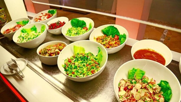 Une table avec différents bols contenant de la salade et un bol de sauce.