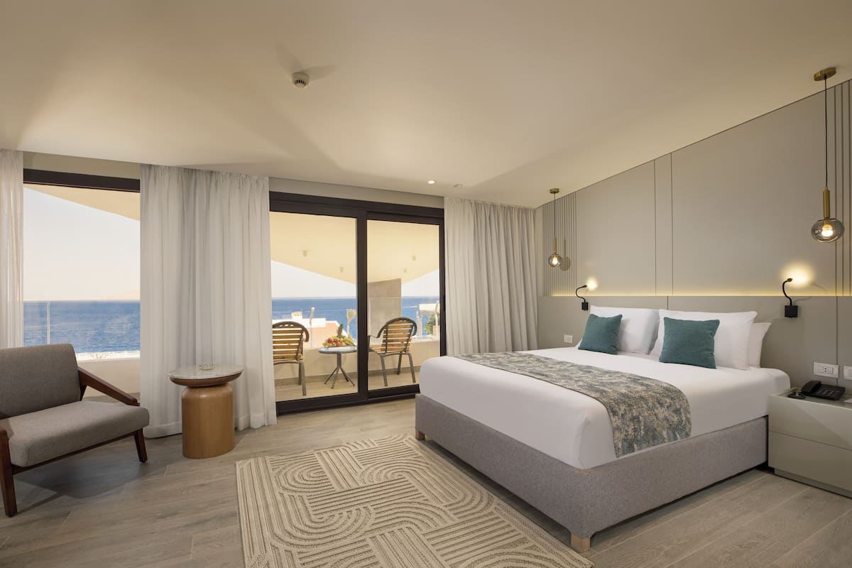Una habitación de hotel moderna con una cama grande, una zona de estar con una mesa y sillas, y un balcón con vistas al océano.