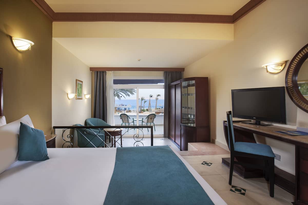 Habitación de hotel con cama, escritorio, televisor y vista a la playa.