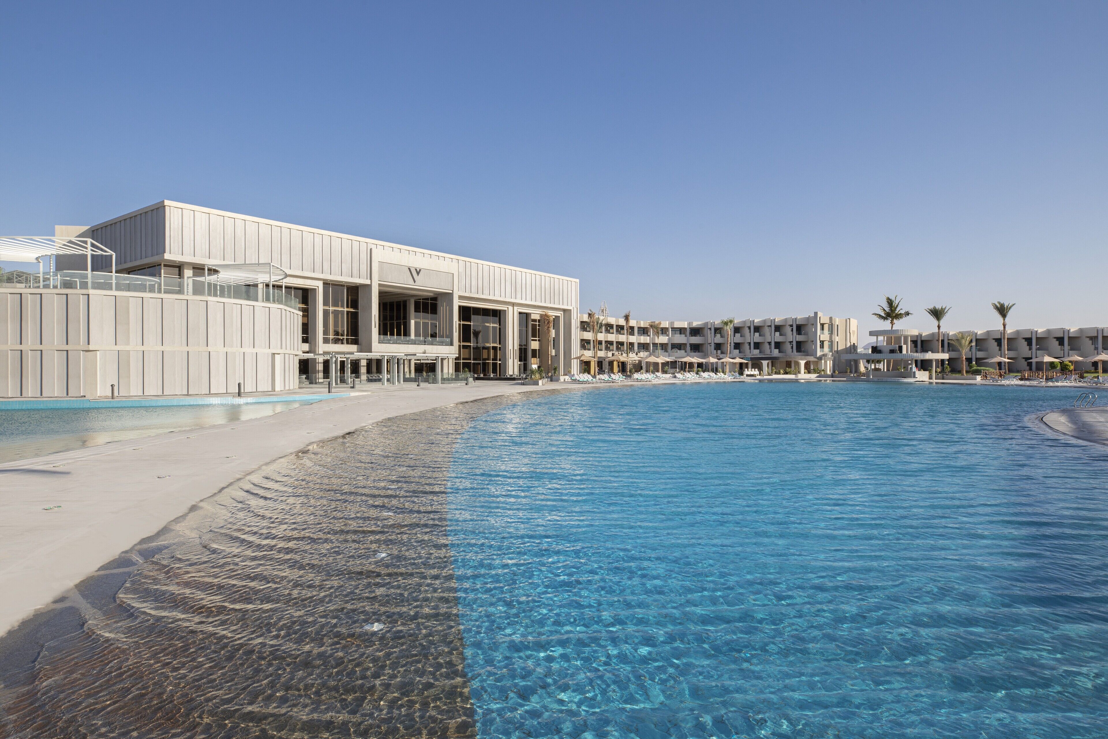 Un hotel modern amb piscina, aigua blava cristal·lina i una zona de platja amb sorra.