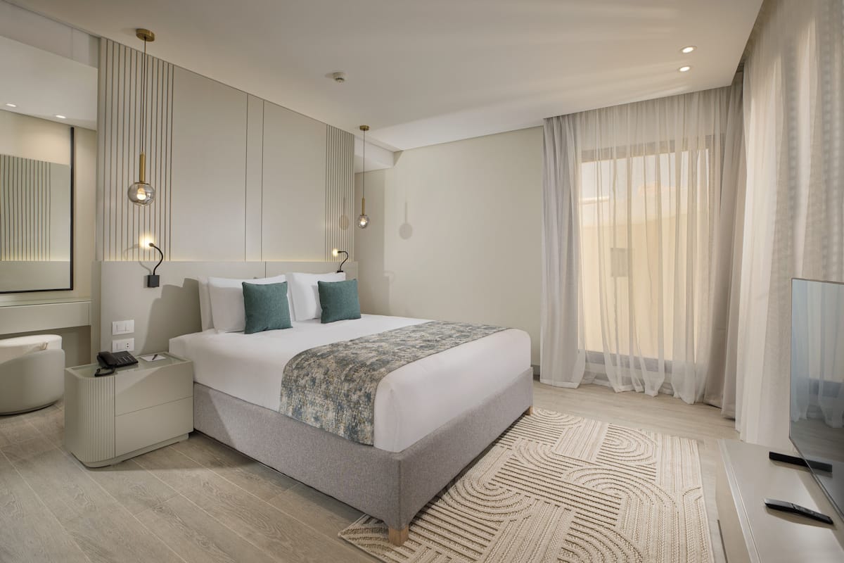 Una habitación de hotel moderna con una cama grande, mesitas de noche, un espejo y un televisor.