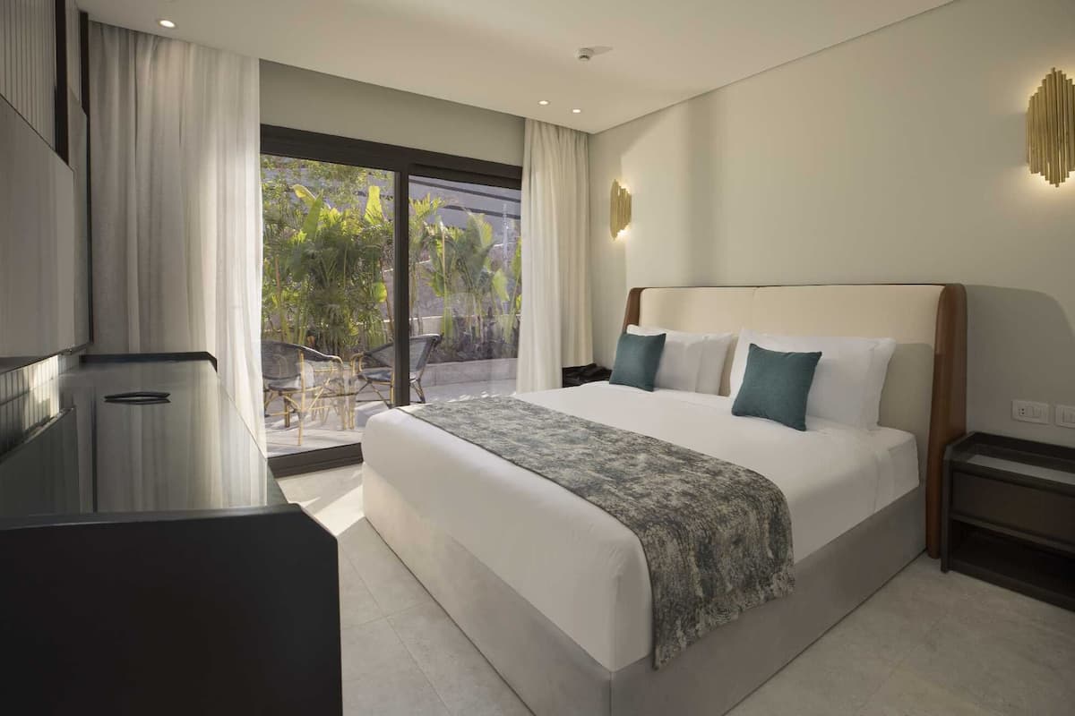 Una habitación de hotel moderna con una cama grande, un escritorio y vistas al exterior a zonas verdes.
