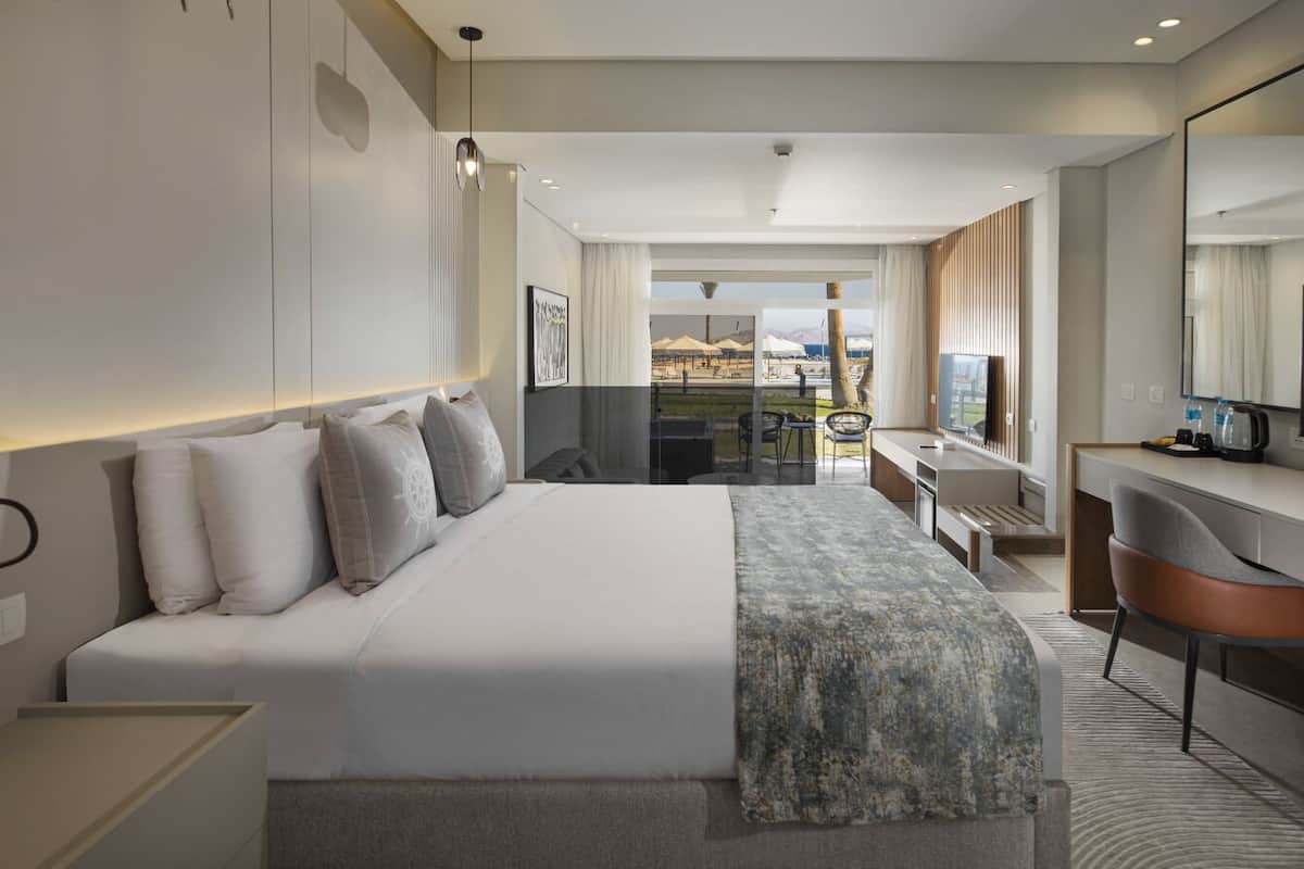 Una habitación de hotel moderna con una cama grande, un escritorio, una silla y vistas al exterior.