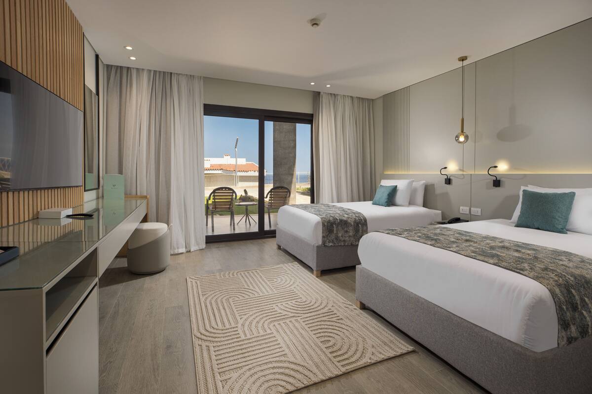 Una habitación de hotel moderna con dos camas, televisión, escritorio y balcón con sillas.