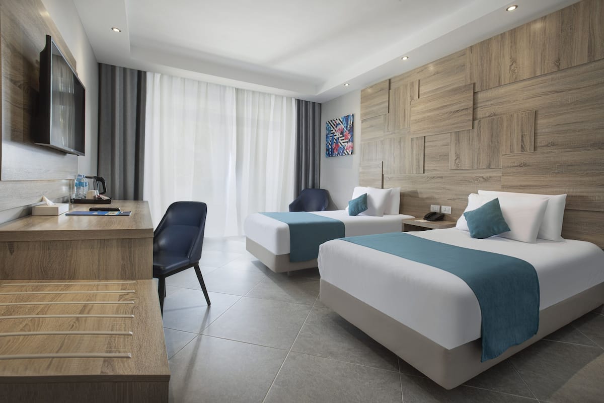 Habitación de hotel con dos camas, un escritorio, una silla, un televisor de pantalla plana y un cuadro en la pared.