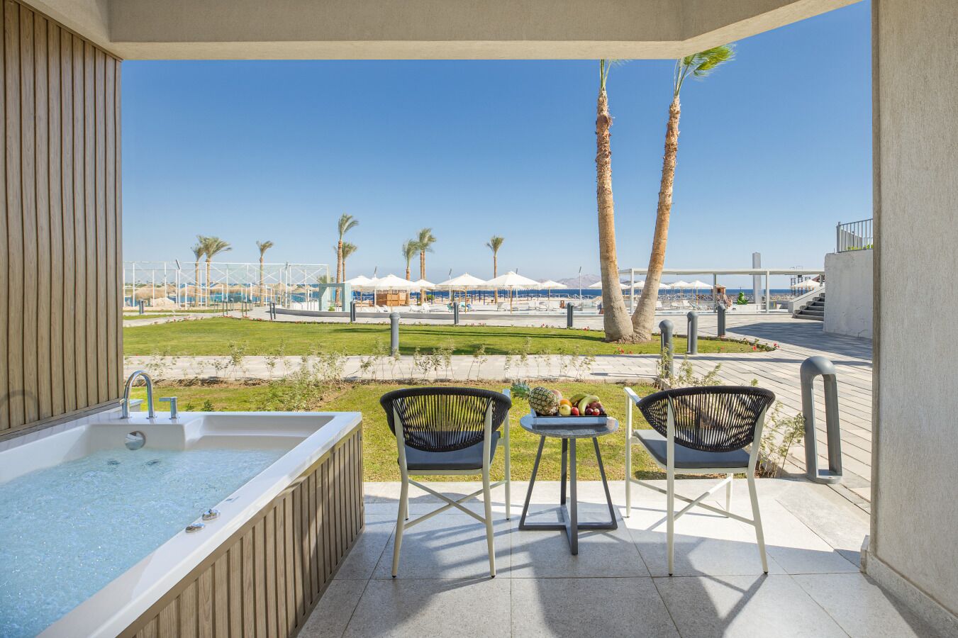 Een balkon met een jacuzzi, twee stoelen en een tafel met fruit.