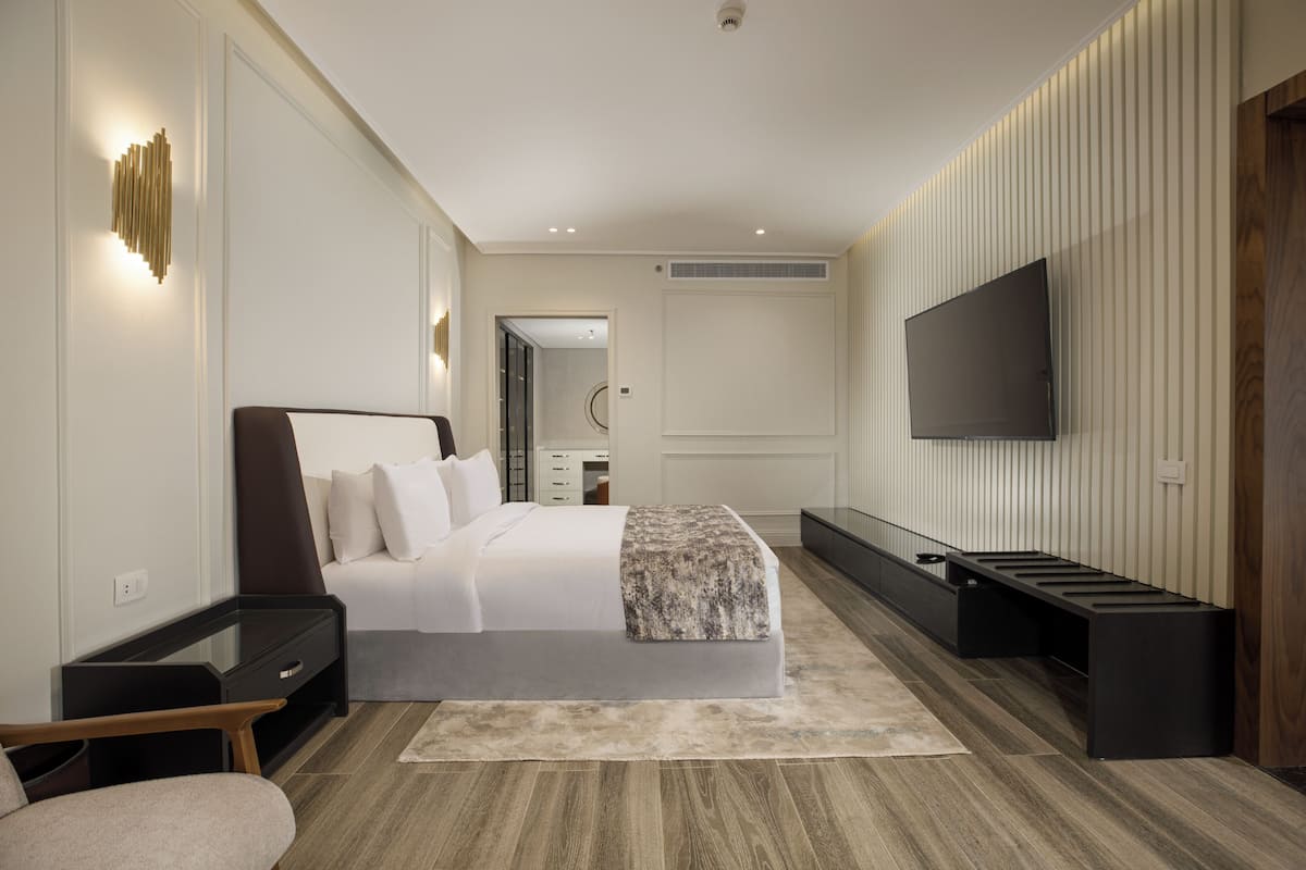 Un dormitorio moderno con cama, mesitas de noche, televisor y un banco.