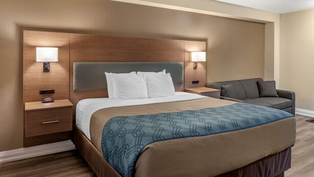A hotel room with a large bed, bedside tables, a nightstand, a sofa, and wall-mounted lamps. - EconoLodge Downtown Toronto (Toronto)